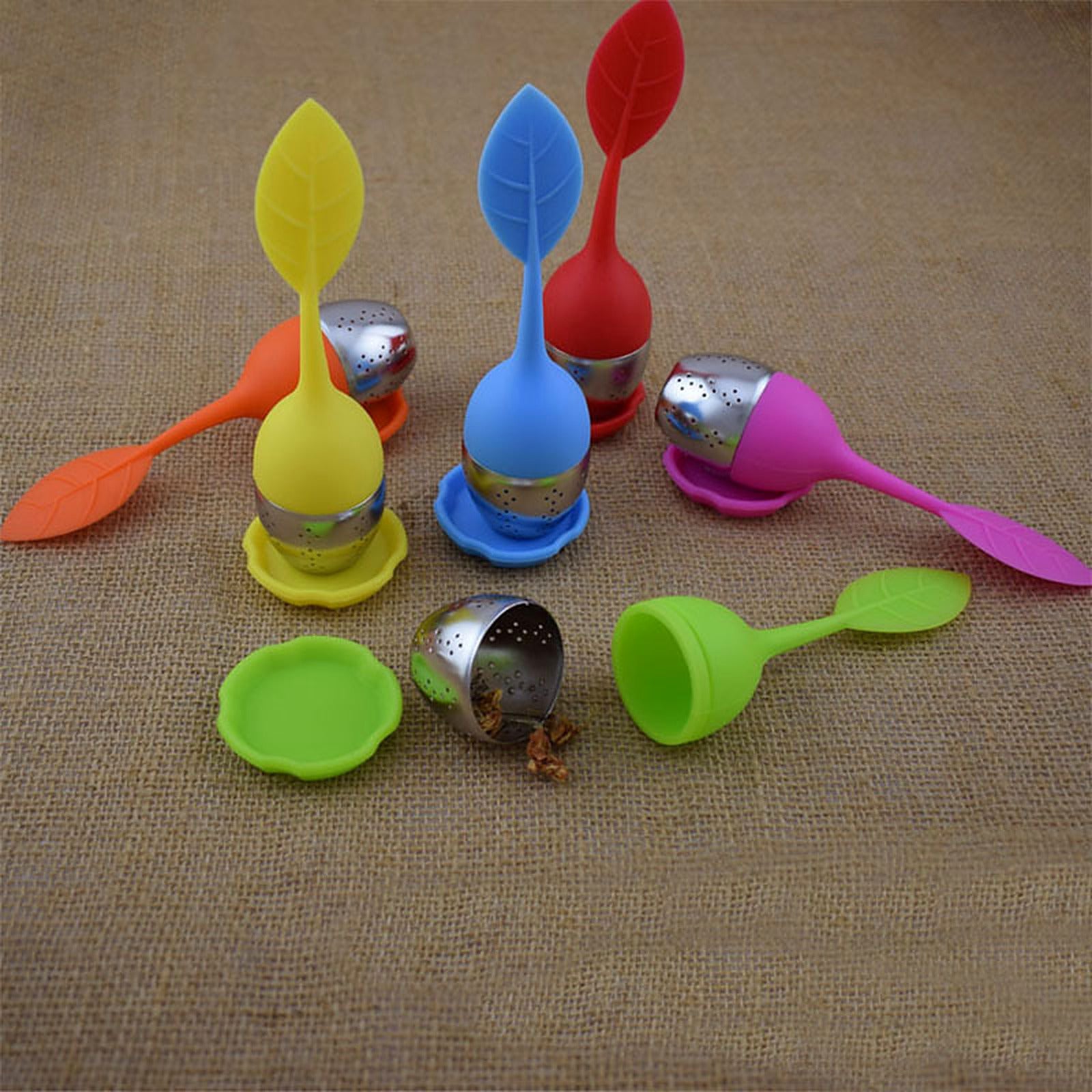 Silicone leaf tea infusers arranged on burlap, one opened to show the stainless steel mesh basket filled with loose leaf tea